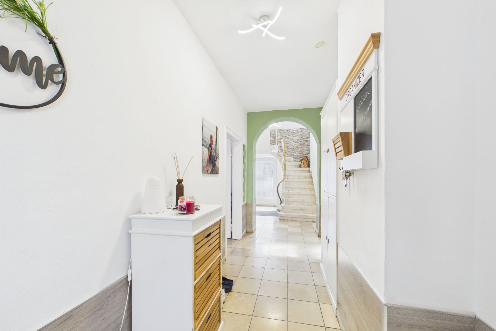 Heller Flur mit Fliesenboden, Kommode links und Treppe im Hintergrund.