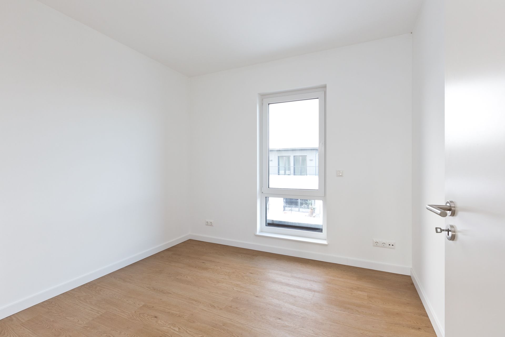 Leeres Zimmer mit weißer Wand, Holzfußboden und großem Fenster.