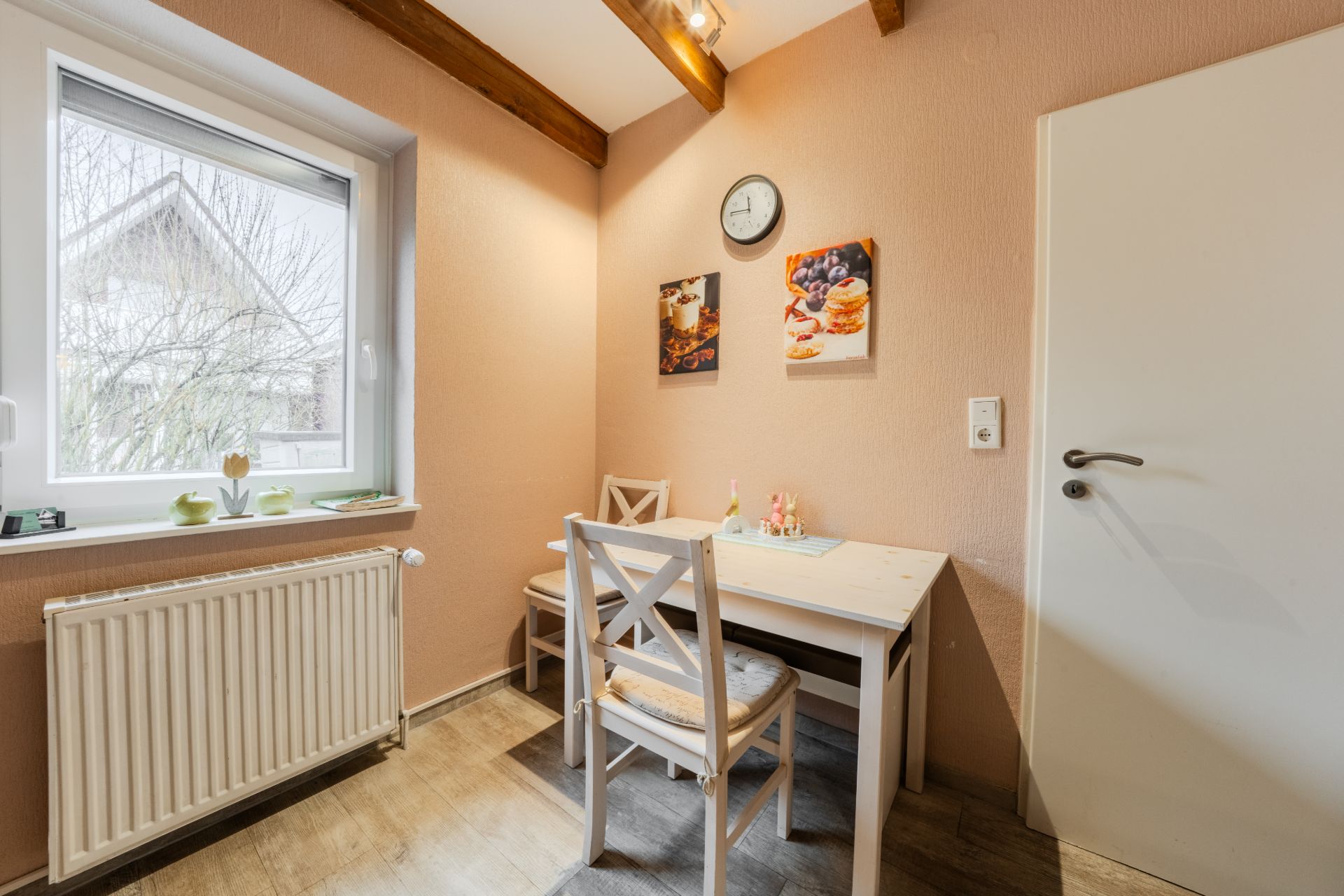 Kleine Essecke mit zwei Stühlen, Tisch, Wandbildern und Fenster mit Blick nach draußen.