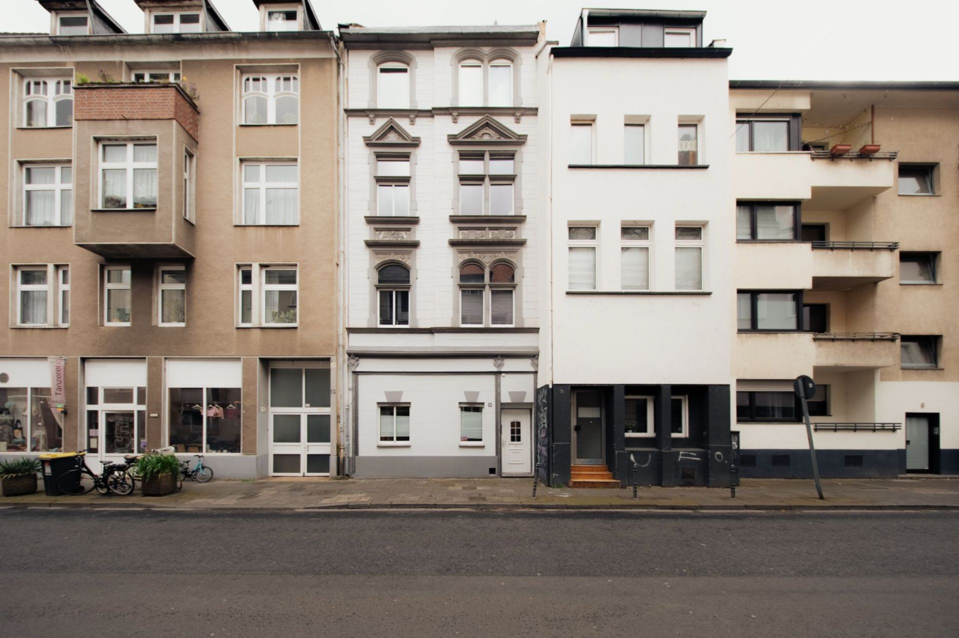 Mehrstöckige Wohnhäuser in einer Reihe an einer ruhigen Straße, Fassaden mit mehreren Fenstern.