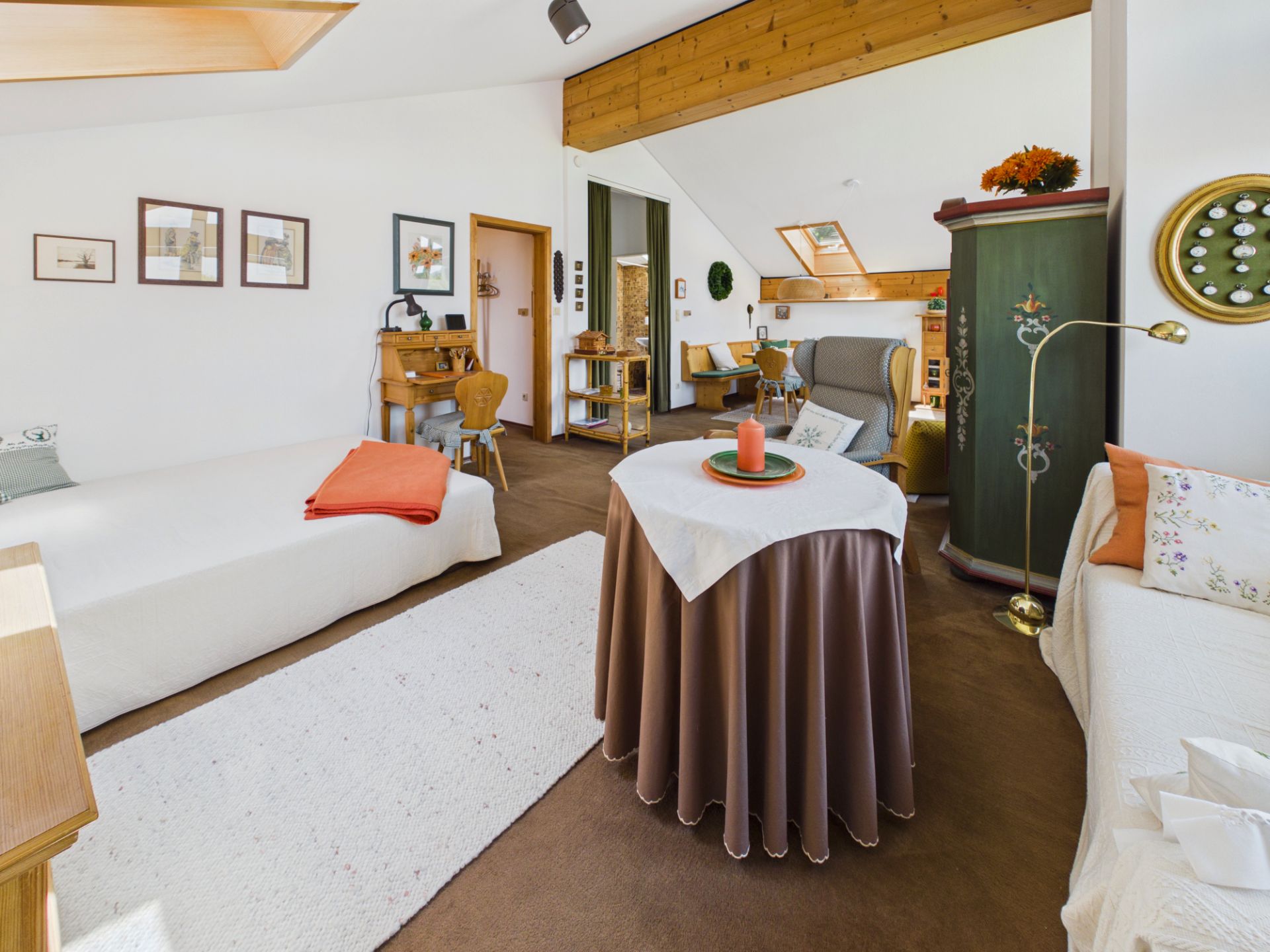 Gemütliches Wohnzimmer mit Betten, Sesseln, Tisch und Schreibtisch, helle Dachfenster.