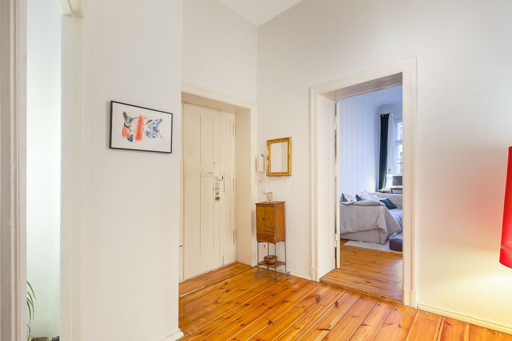 Heller Flur mit Holzboden, einem kleinen Schrank und Blick in ein Schlafzimmer.