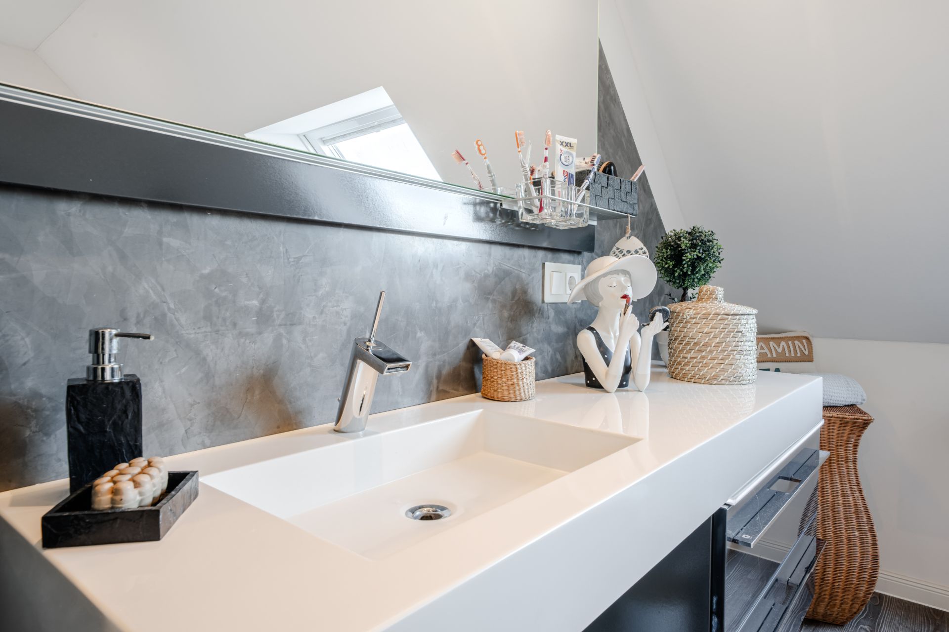 Modernes Badezimmer mit weißem Waschbecken, Spiegel, Dekoration und Zahnbürstenbechern.