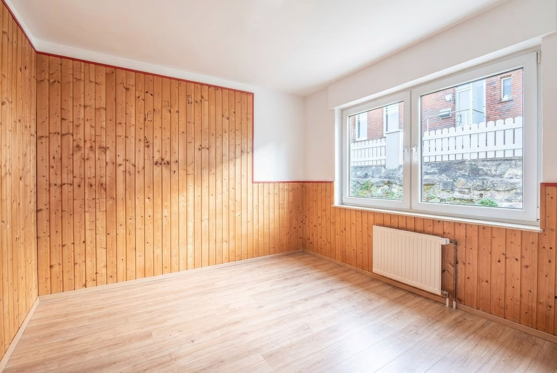 Leerer Raum mit Holzvertäfelung, großem Fenster und Heizung unter dem Fenster.