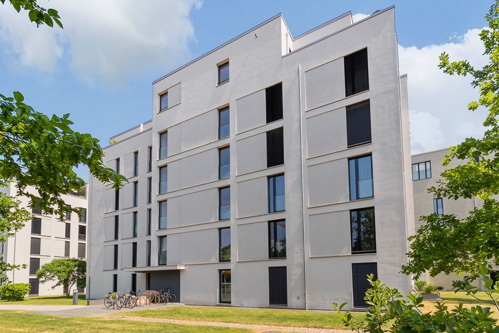 Modernes Wohnhaus mit mehreren Etagen und großen Fenstern, Fahrräder stehen vor dem Gebäude.