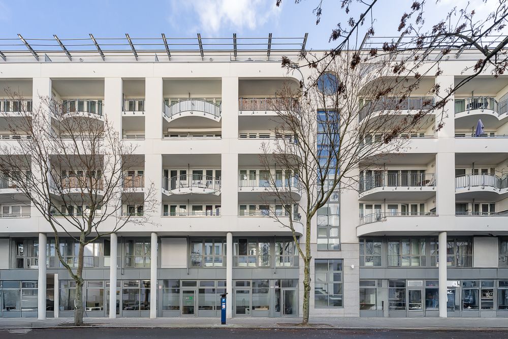 Mehrstöckiges Wohngebäude mit Balkonen, großen Fenstern und kahlen Bäumen davor.