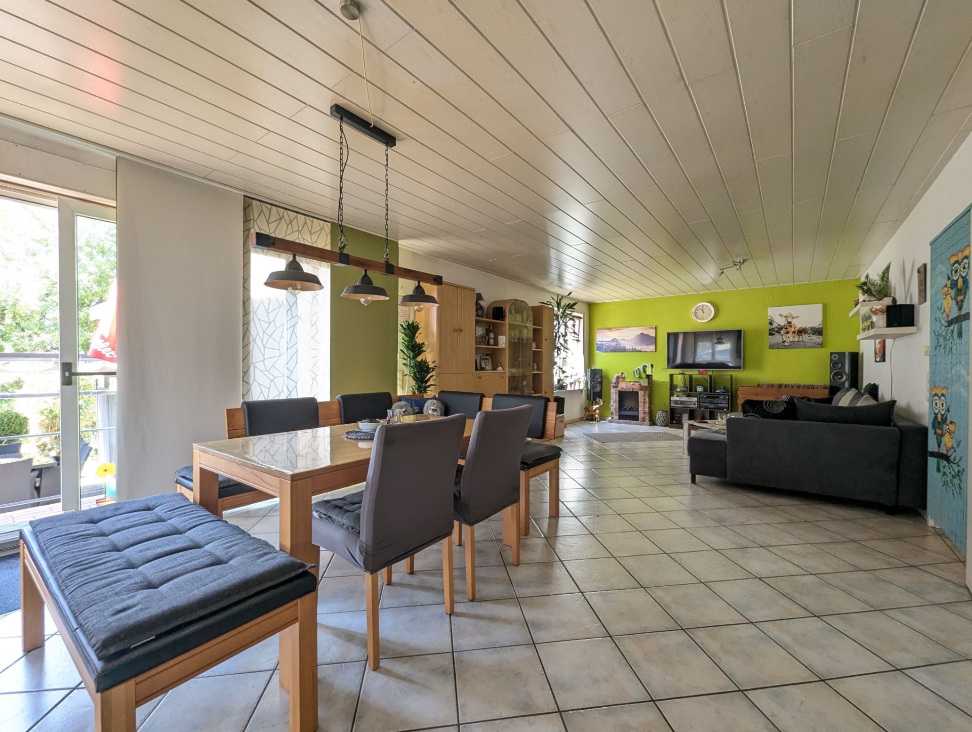 Helles Wohnzimmer mit Esstisch, Stühlen, Sofa, TV und Zugang zum Balkon.