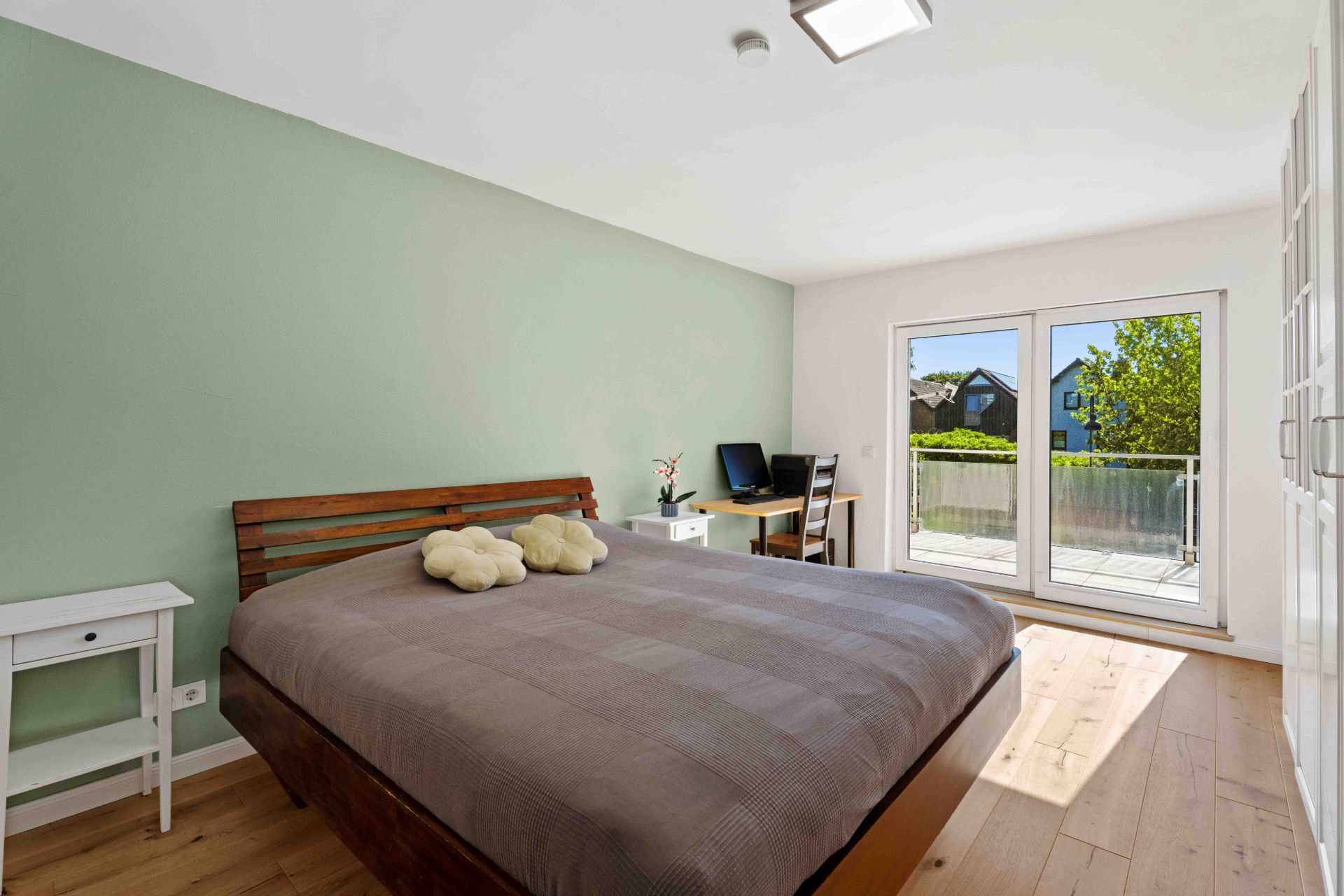 Helles Schlafzimmer mit Doppelbett, Schreibtisch und Zugang zu einem Balkon durch große Glastüren.
