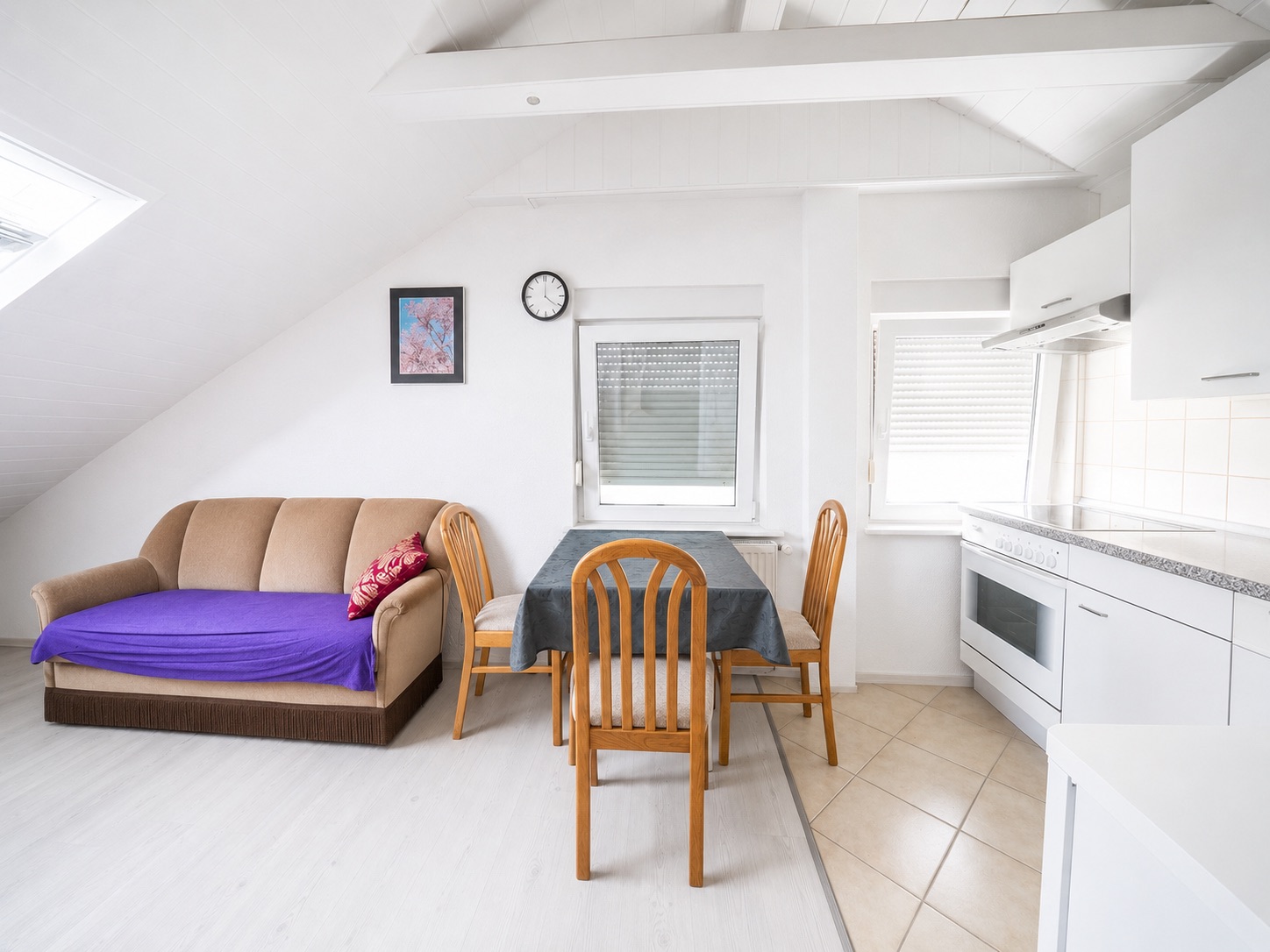 Heller Wohnraum mit Sofa, Esstisch, vier Stühlen und moderner Einbauküche.