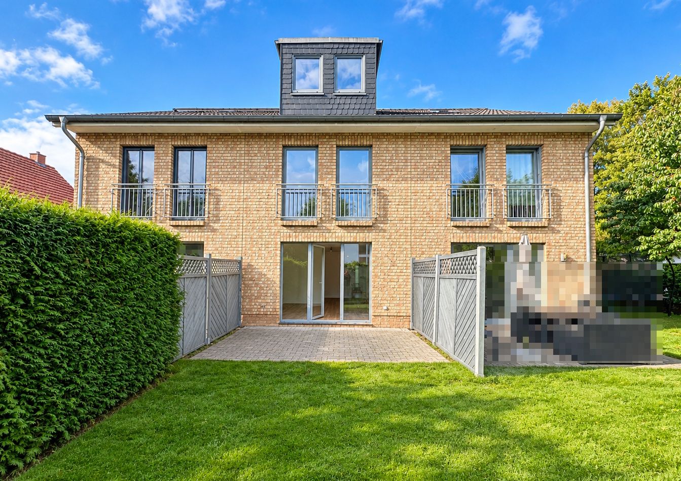 Backstein-Doppelhaushälfte mit Balkon und Terrasse, Garten und Hecke im Vordergrund.