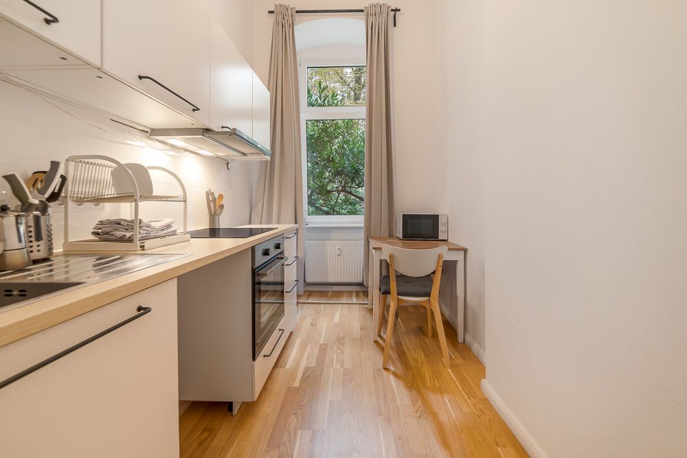 Helle Einbauküche mit Holzarbeitsplatte, kleinem Tisch, Stuhl und Fenster mit Vorhängen.