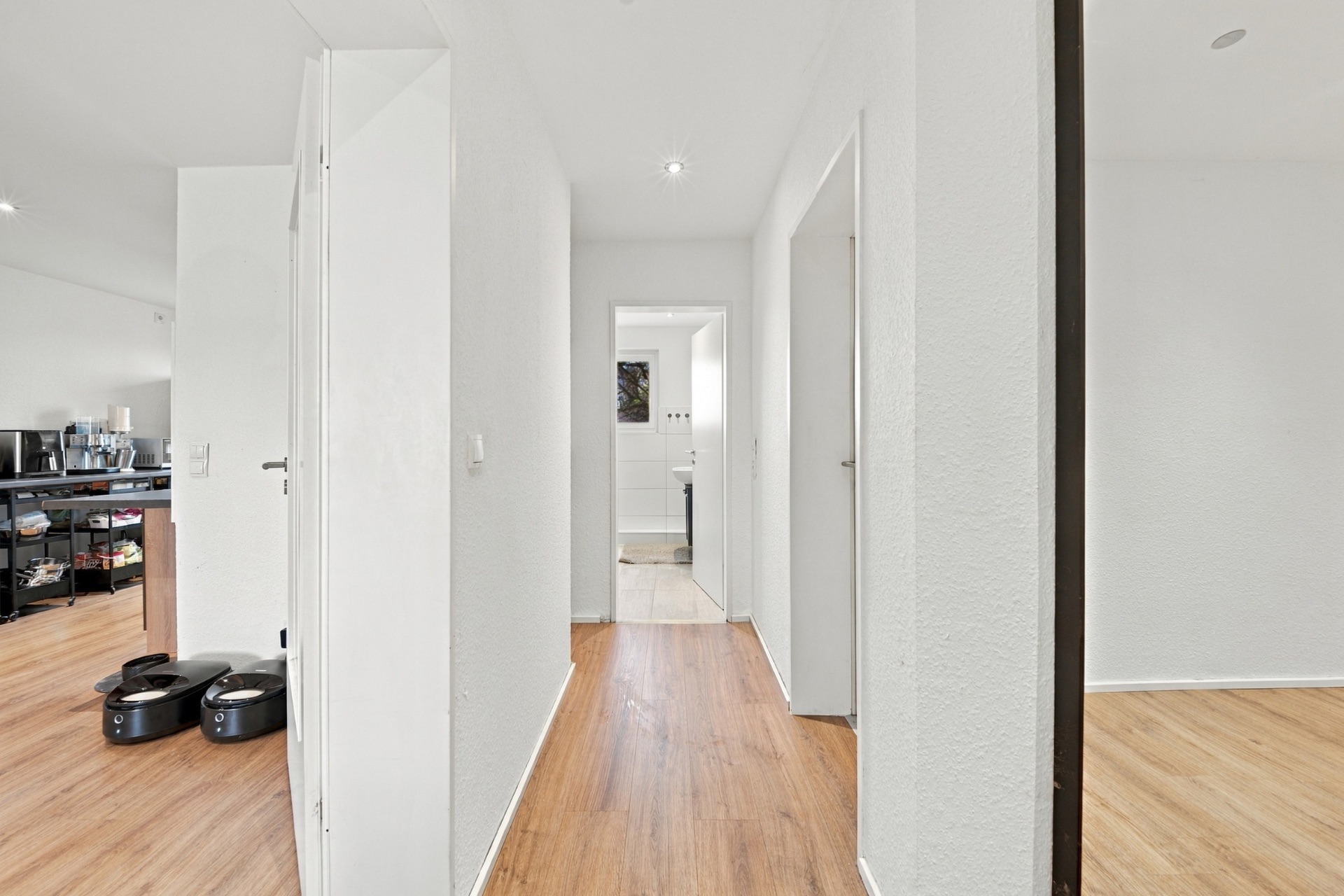 Heller Flur mit Holzboden, mehreren Türen und Sicht auf ein Badezimmer.