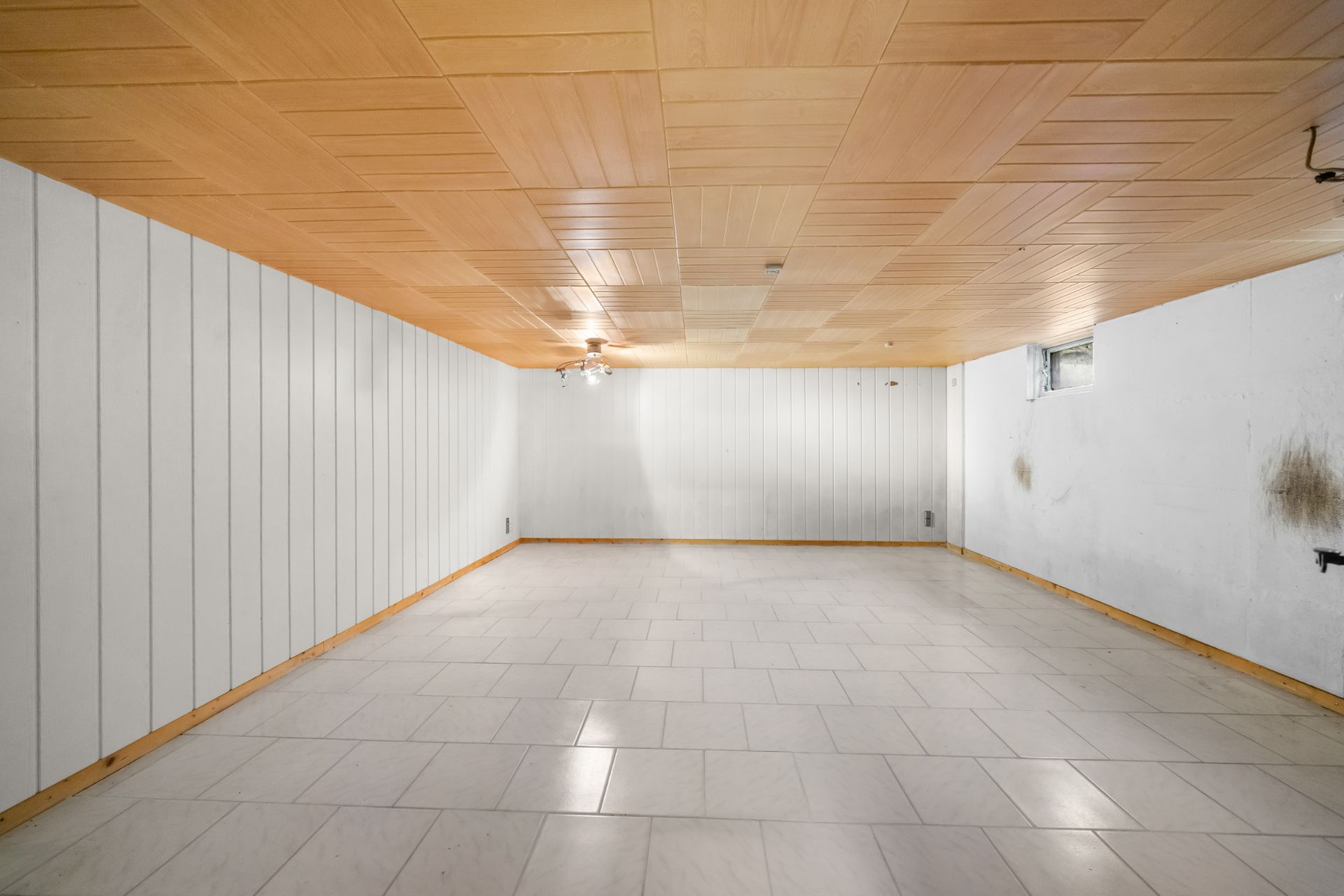 Leerer Kellerraum mit weiß gefliesten Böden und holzverkleideter Decke.