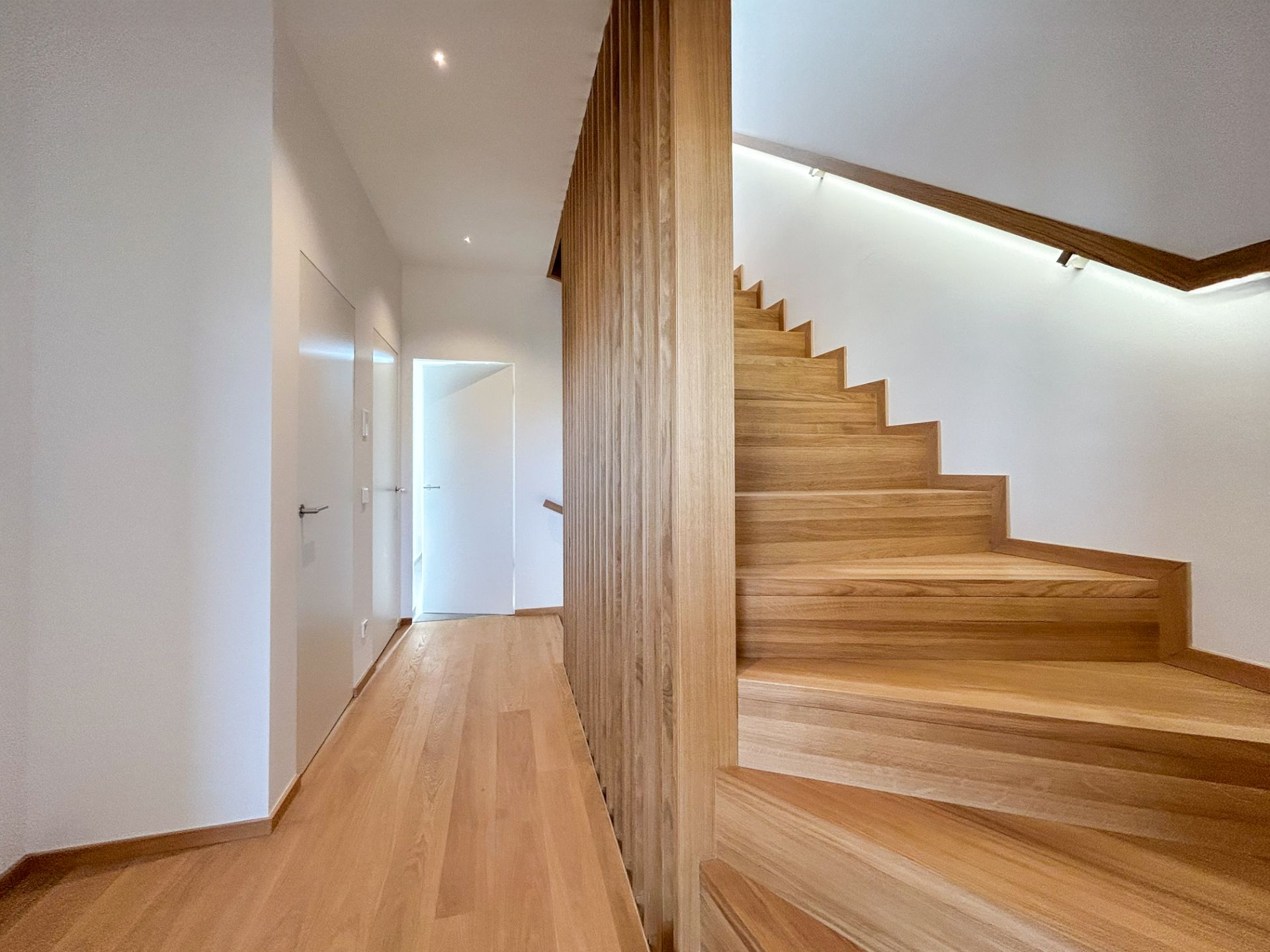 Heller Flur mit Holztreppe und weißen Türen, modernes Design.