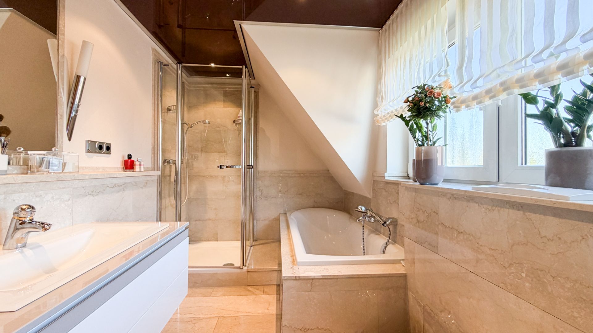 Modernes Badezimmer mit Badewanne, Dusche, Waschbecken und großen Fenstern mit Blumen auf der Fensterbank.