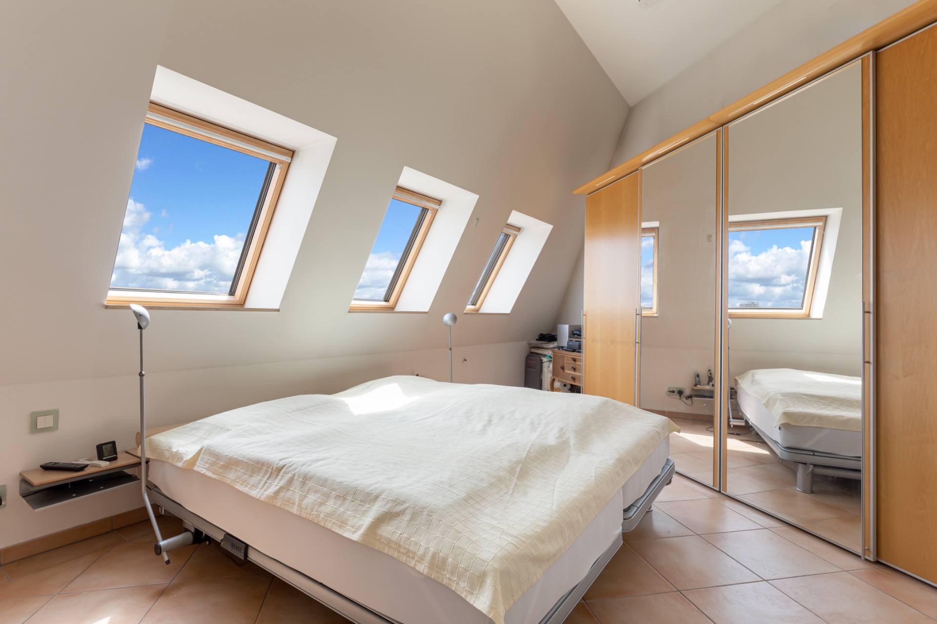 Helles Schlafzimmer mit Dachfenstern, Doppelbett und großem Spiegelschrank.