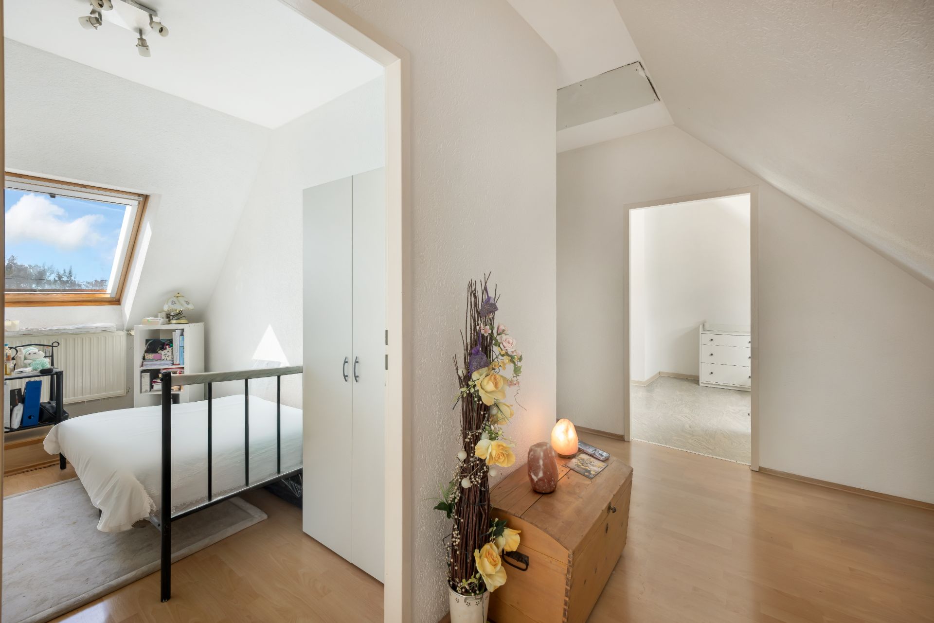 Flur mit Truhe und Blumendeko, Blick in ein Schlafzimmer mit Bett und Dachfenster.