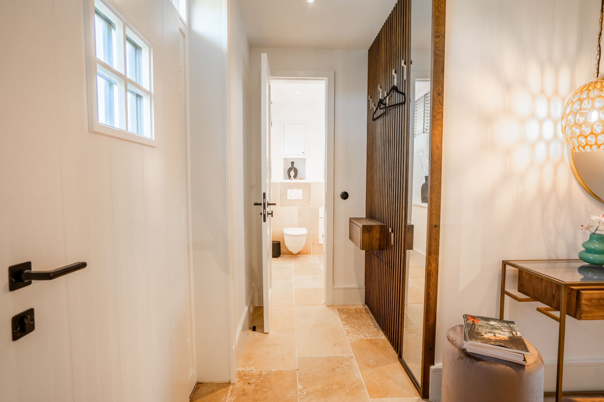 Heller Flur mit Blick ins Badezimmer, Spiegel, Holztisch und dekorativer Lampe.