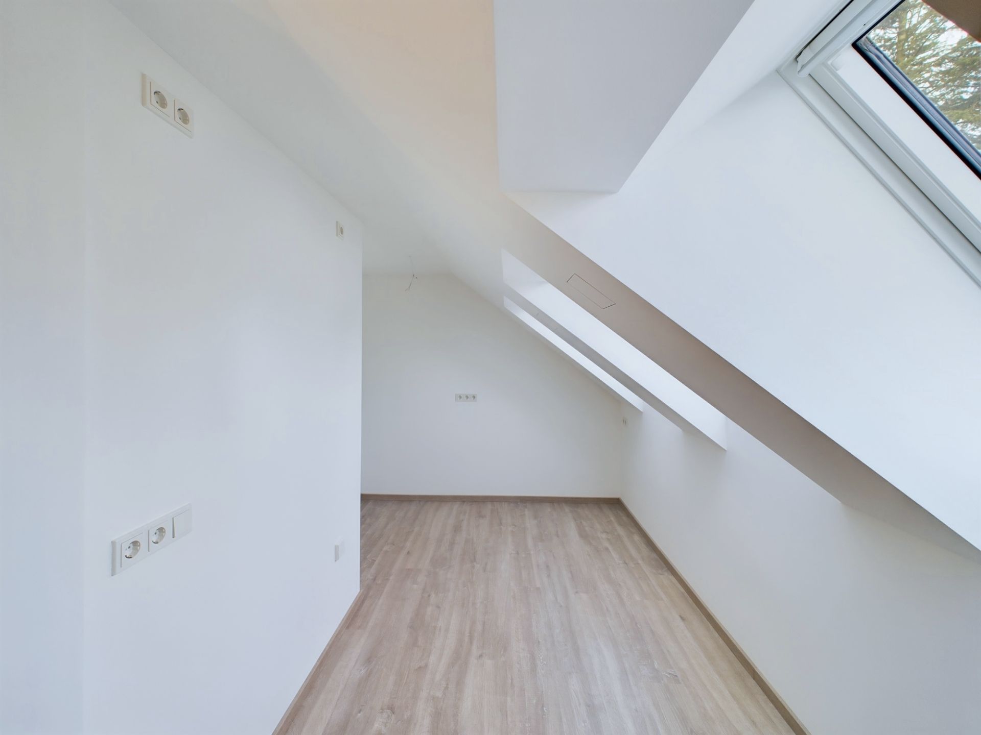 Heller Dachraum mit schrägen Fenstern, weiß gestrichenen Wänden und Holzfußboden.