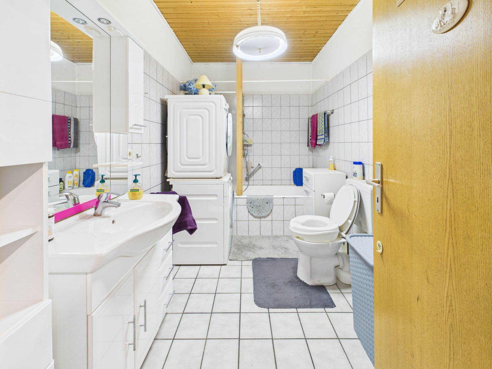 Helles Badezimmer mit Waschbecken, Toilette, Badewanne, Waschmaschine und Trockner.