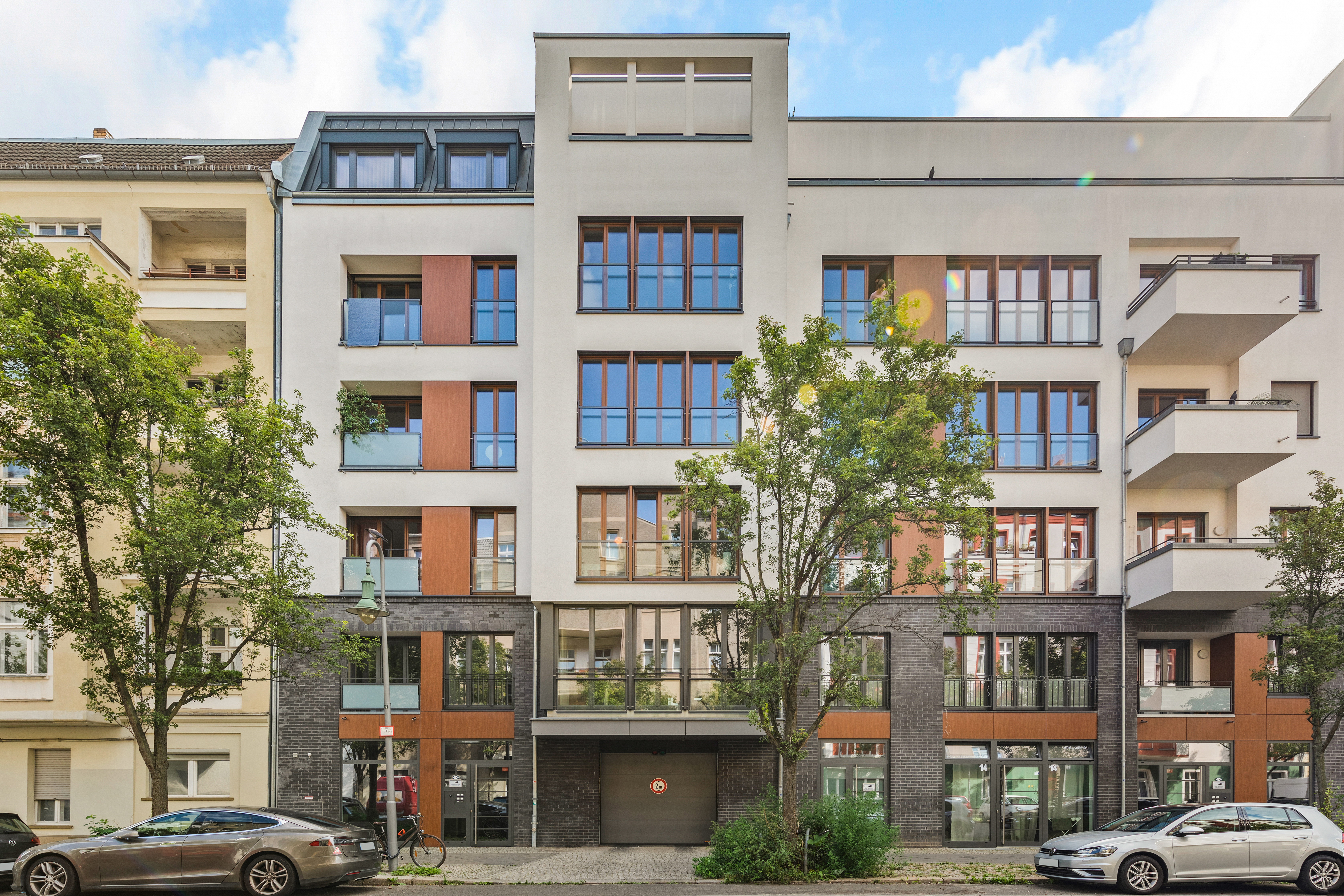 Moderne Wohnhausfassade mit großen Fenstern, Balkonen und zwei Bäumen davor.