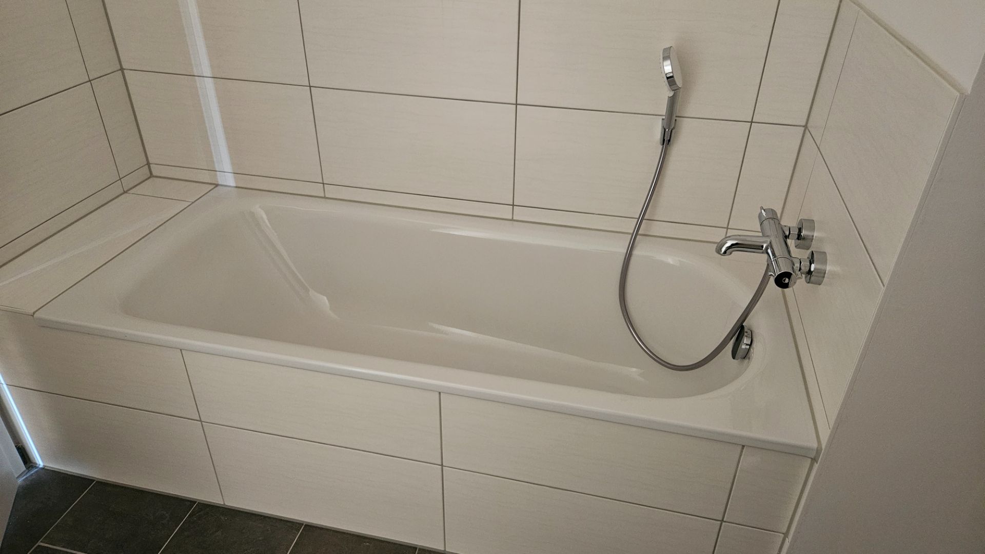Weiße Badewanne mit Fliesenwand und Handbrause in einem Badezimmer.