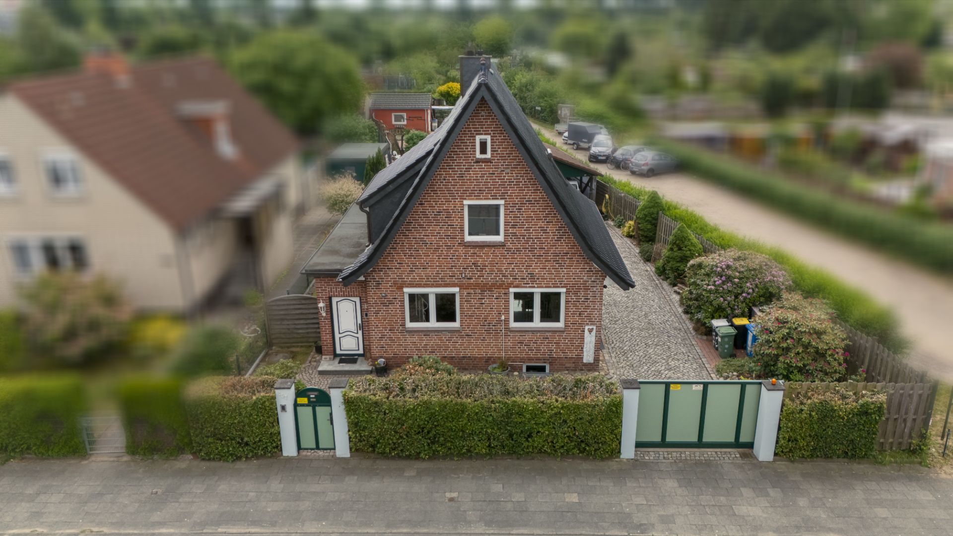 Backsteinhaus mit spitzem Dach, Garten und Zaun an einer Wohnstraße.