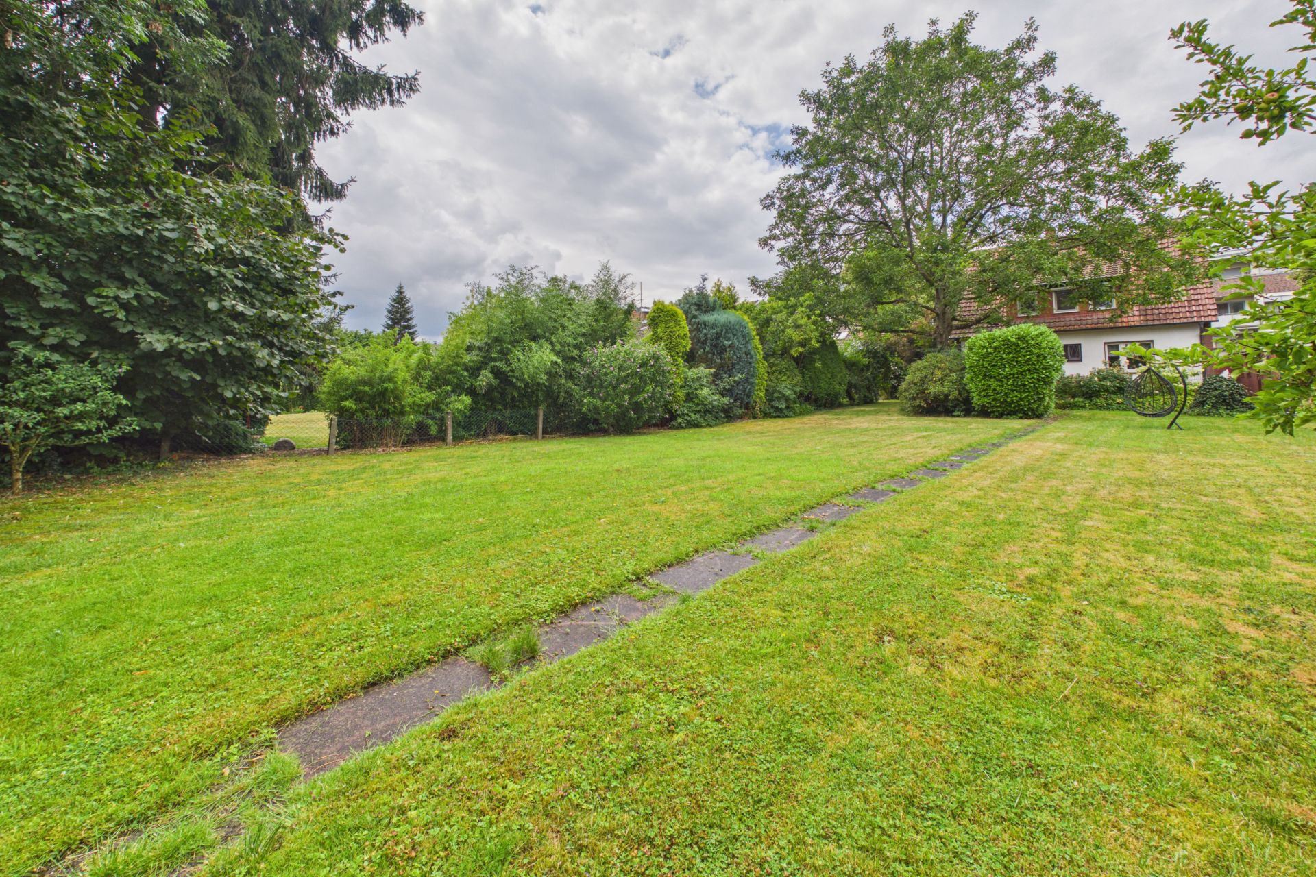 Großer grüner Garten mit Rasen, Bäumen und einem Haus im Hintergrund.
