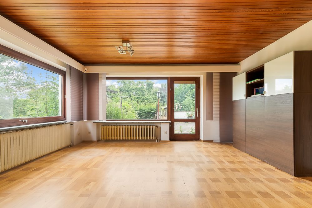 Helles Wohnzimmer mit großen Fenstern, Holzboden, Holzdecke und Einbauschränken.