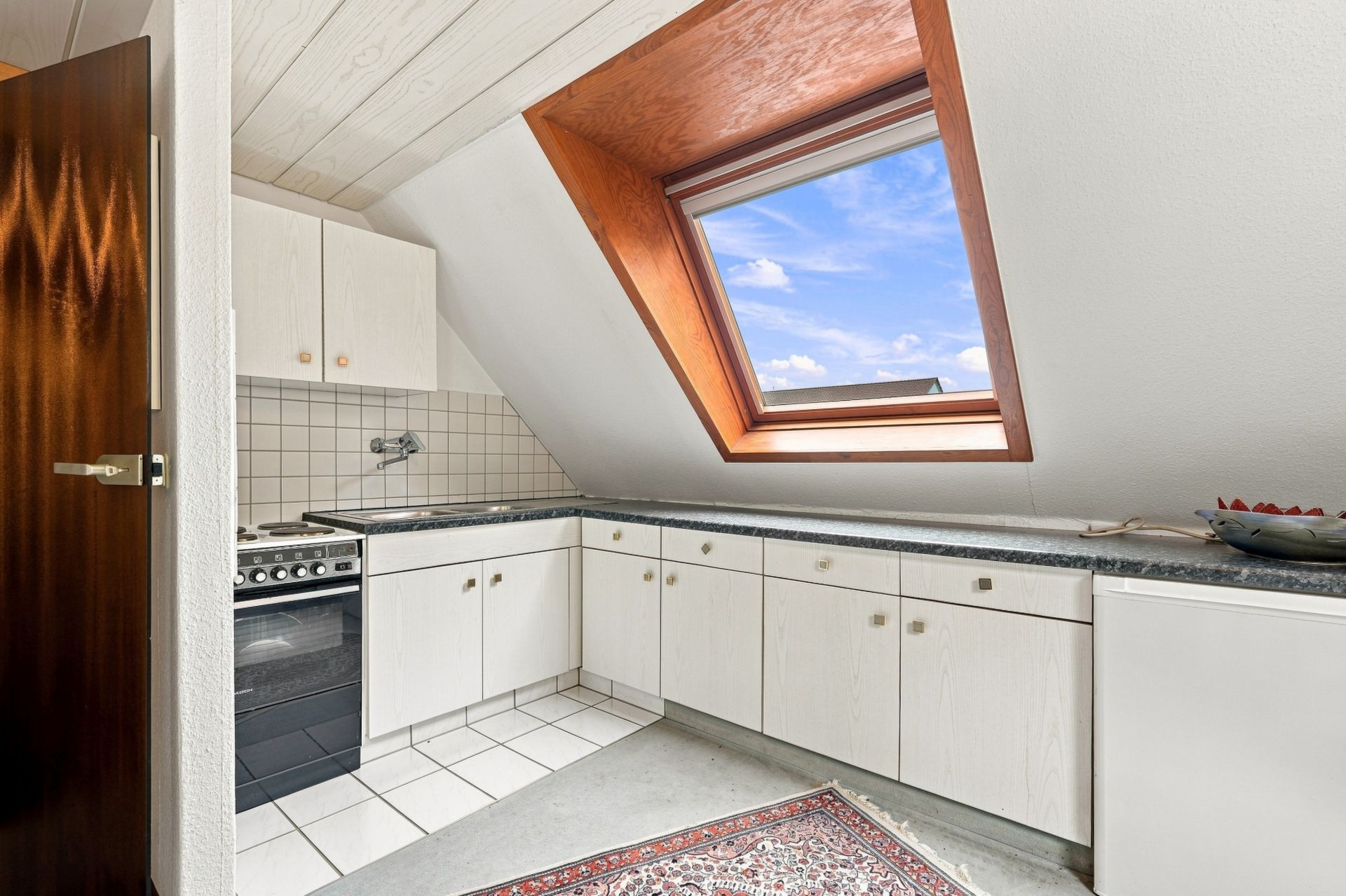 Helle Küche mit weißem Schrank, Dachfenster und Teppich auf dem Boden.