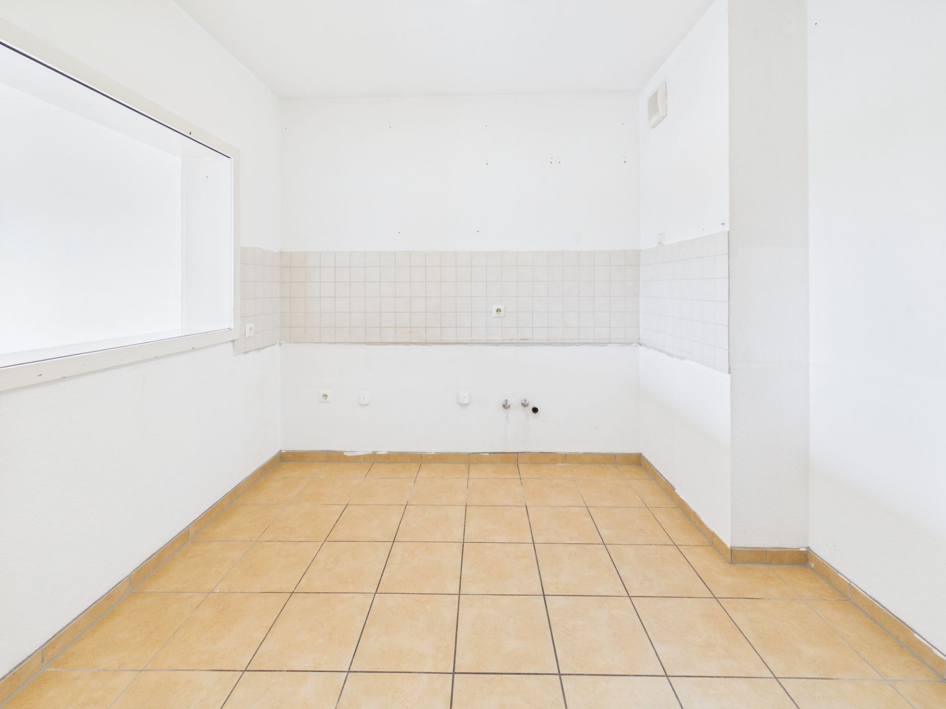 Leerer, gefliester Raum mit weiß gefliesten Wänden und großem Fenster.