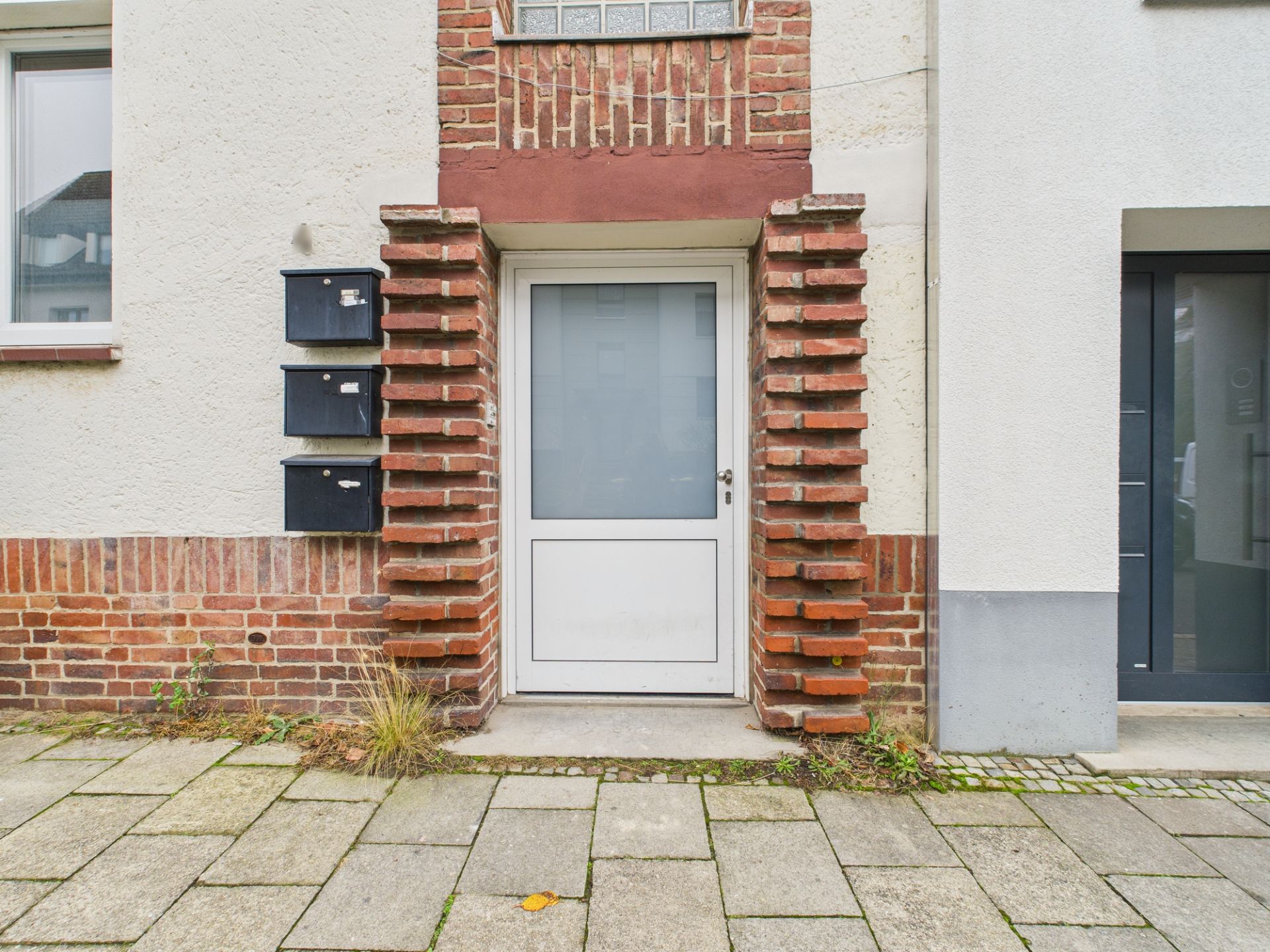 Eingangstür mit Glasfenster, von roten Ziegelsteinen eingerahmt, und drei schwarze Briefkästen daneben.