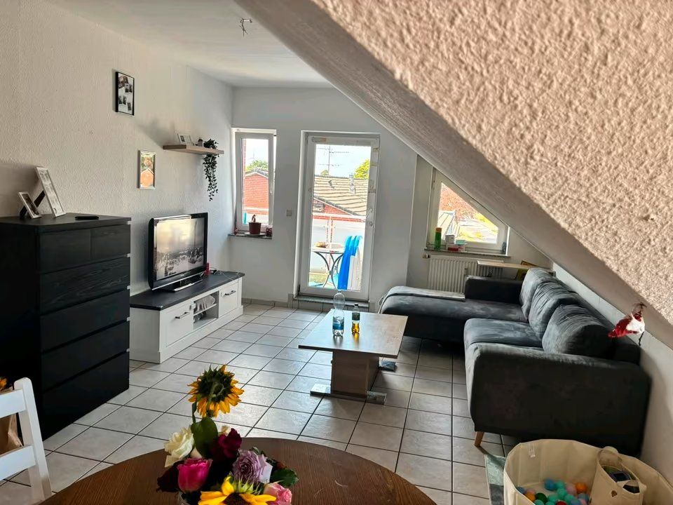 Wohnzimmer mit Ecksofa, Couchtisch, Fernseher, Kommode und Zugang zum Balkon.