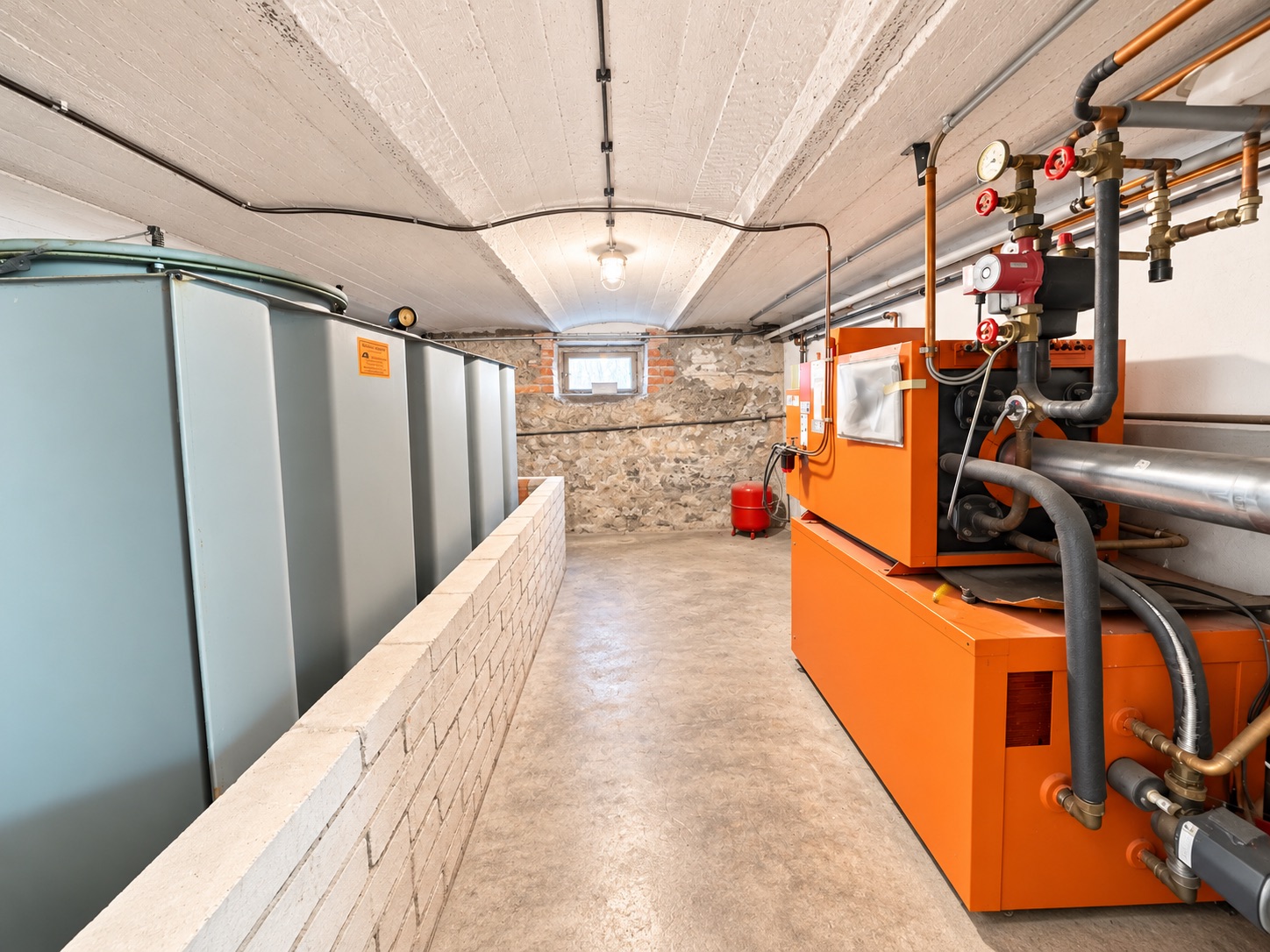 Heizungsraum mit Öltanks und oranger Heizungsanlage im Keller eines Wohnhauses.