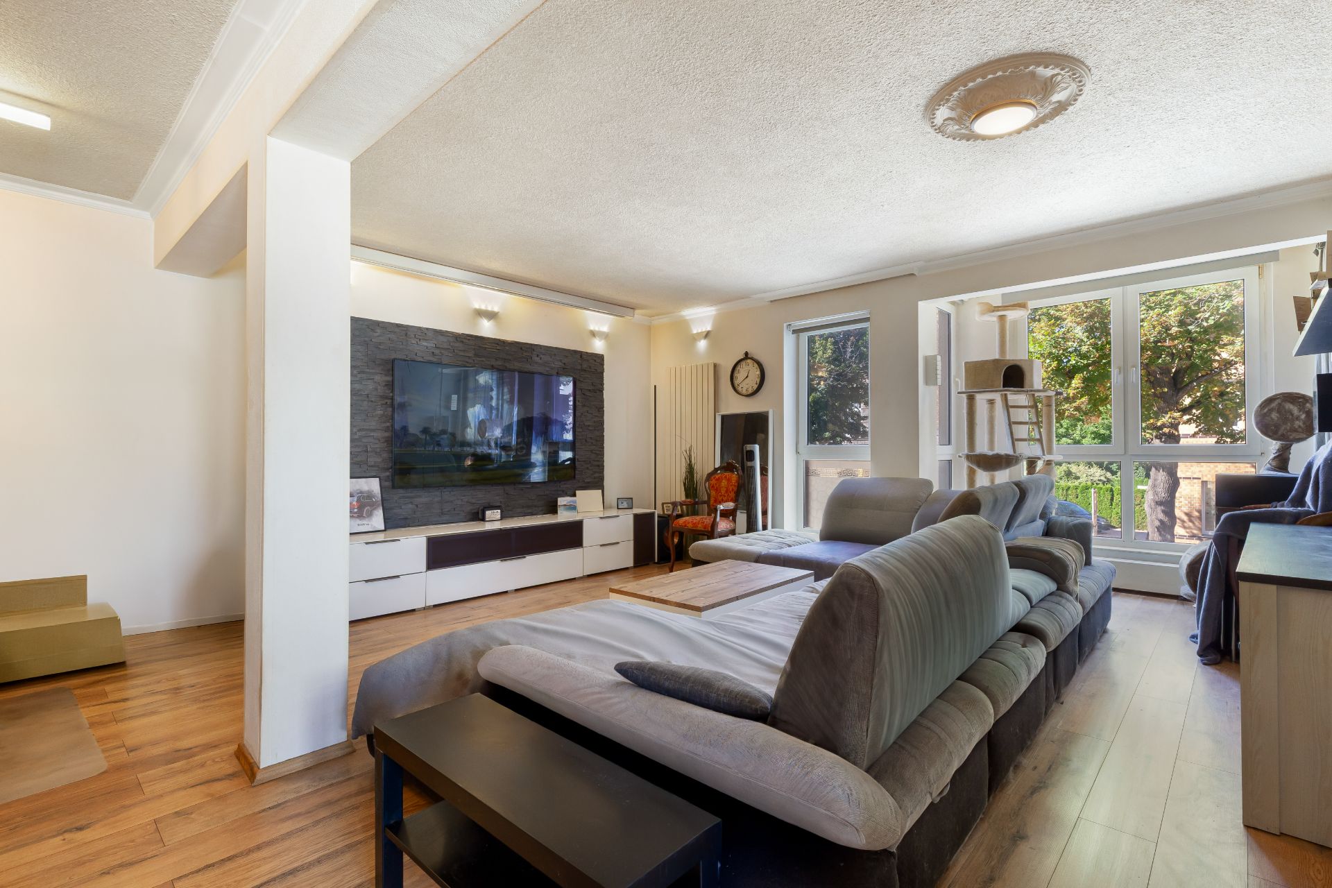 Modernes Wohnzimmer mit großem Sofa, TV-Wand und bodentiefen Fenstern zum Balkon.