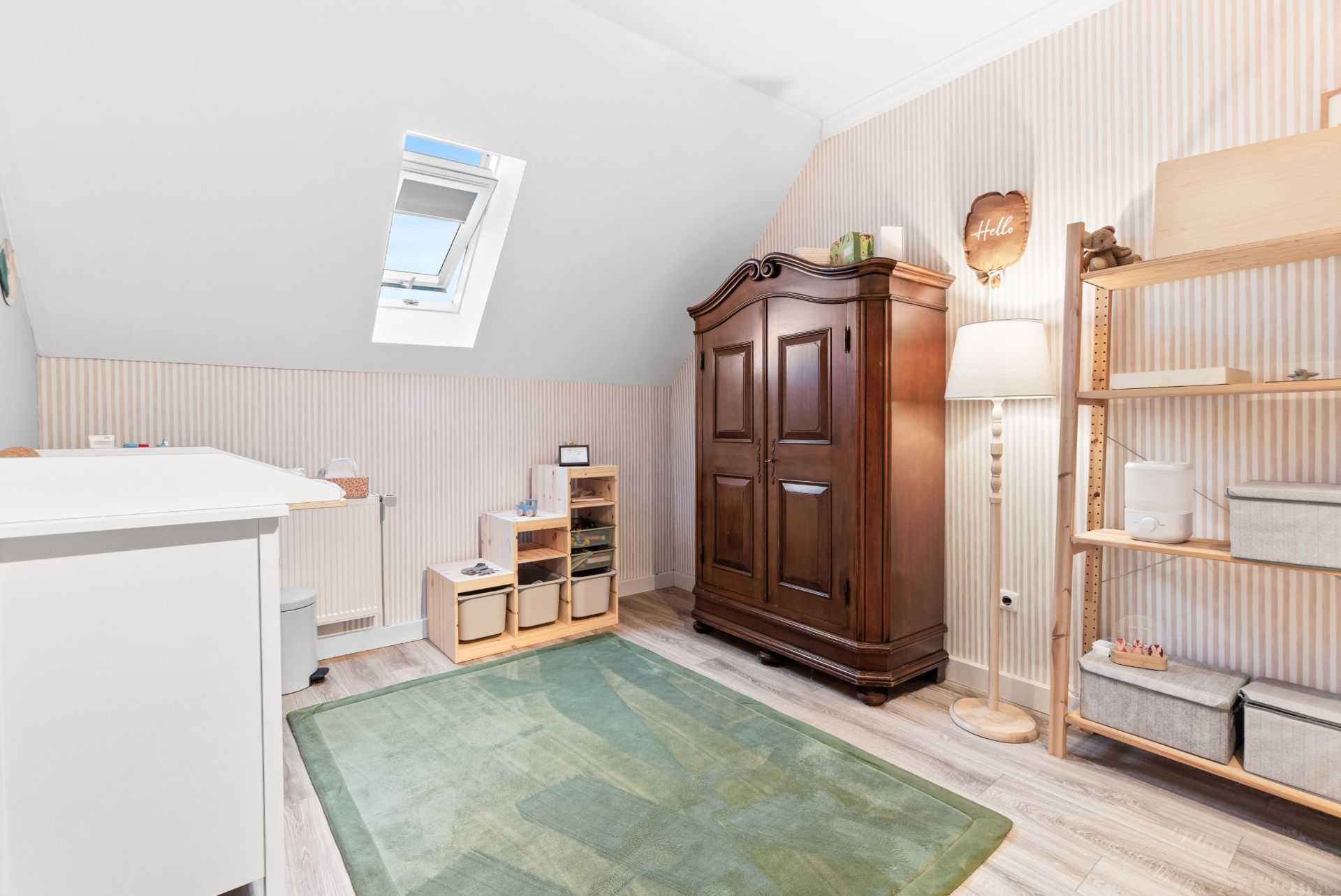 Helles Zimmer mit Dachfenster, grünem Teppich, Holzschrank, Regal und Kommoden.