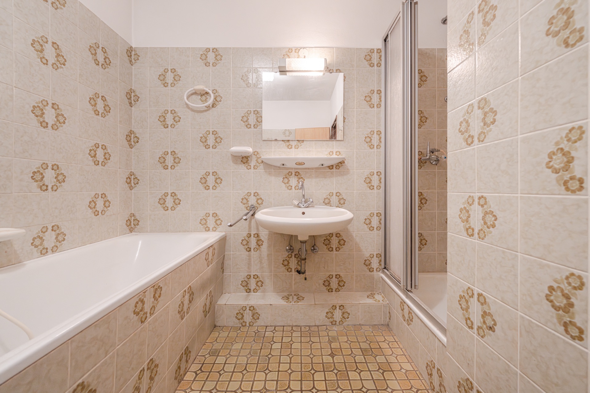 Kleines Badezimmer mit Badewanne, Waschbecken und gemusterten Fliesen an Wand und Boden.