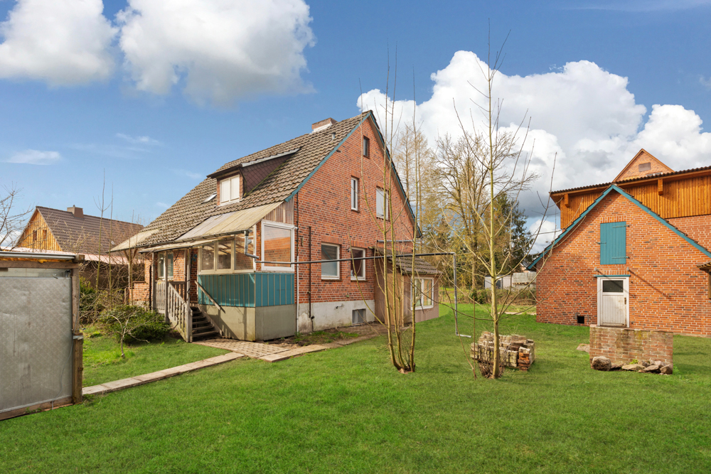 Ziegelhaus mit Wintergarten, Garten und Nebengebäude an einem sonnigen Tag.