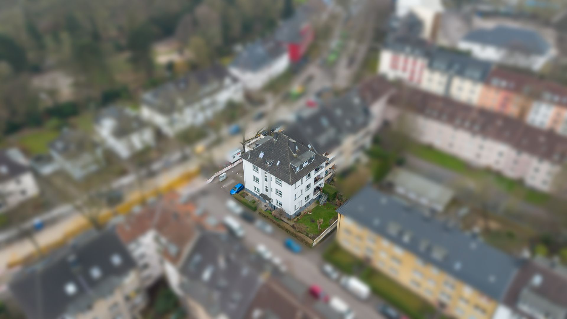 Luftaufnahme eines weißen Mehrfamilienhauses mit Garten inmitten anderer Wohngebäude.