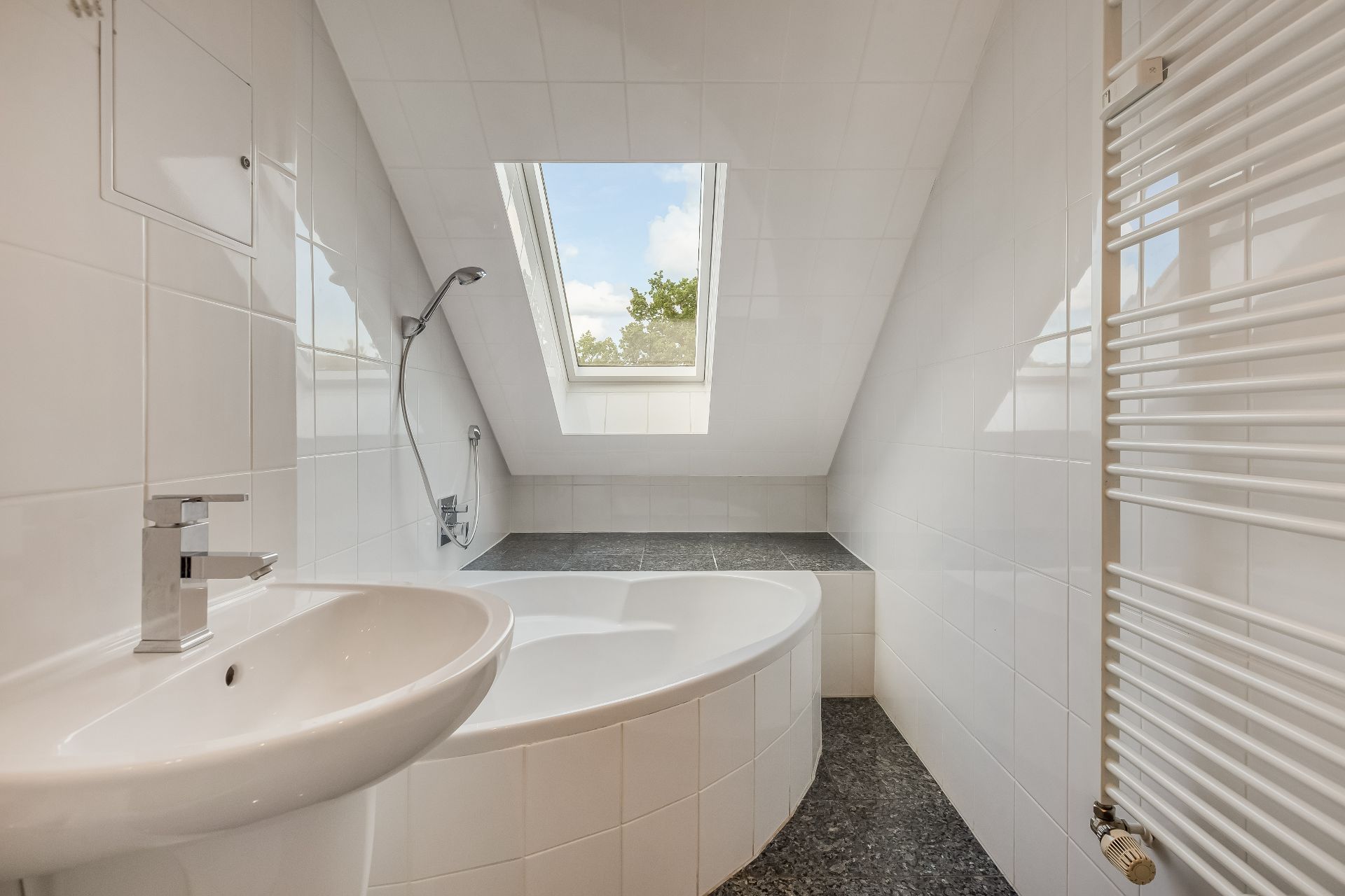 Modernes Badezimmer mit Badewanne, Waschbecken und Dachfenster unter einer Schräge.