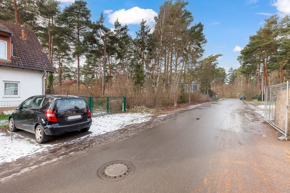 Straße mit geparktem Auto und Haus am Rand, leichte Schneedecke, Bäume im Hintergrund.