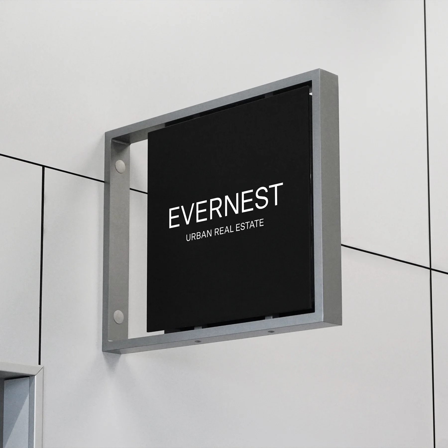 Schwarzes Schild mit weißer Aufschrift 'EVERNEST URBAN REAL ESTATE' an einer hellen Wand.