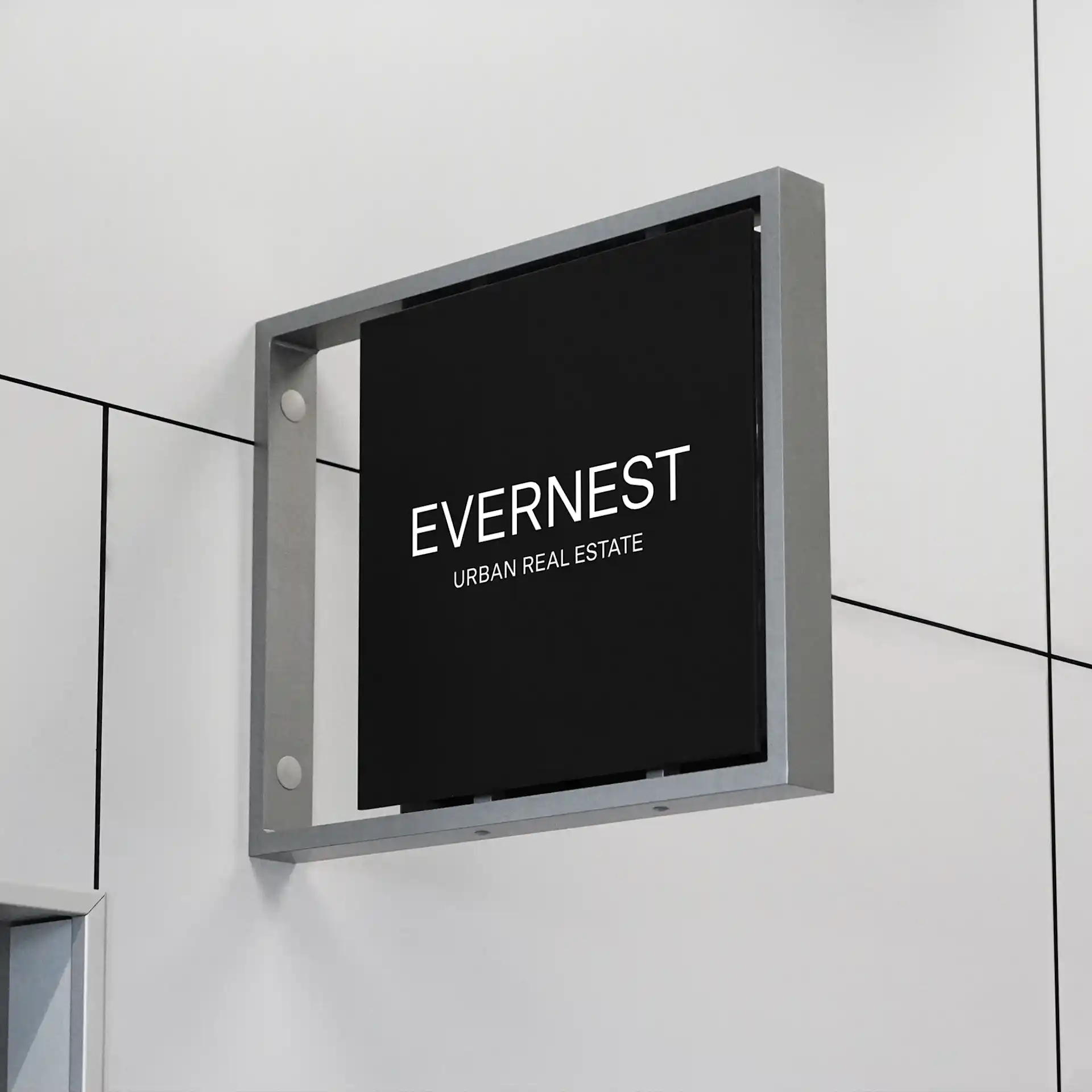 Schwarzes Schild mit weißer Aufschrift 'EVERNEST URBAN REAL ESTATE' an einer hellen Wand.