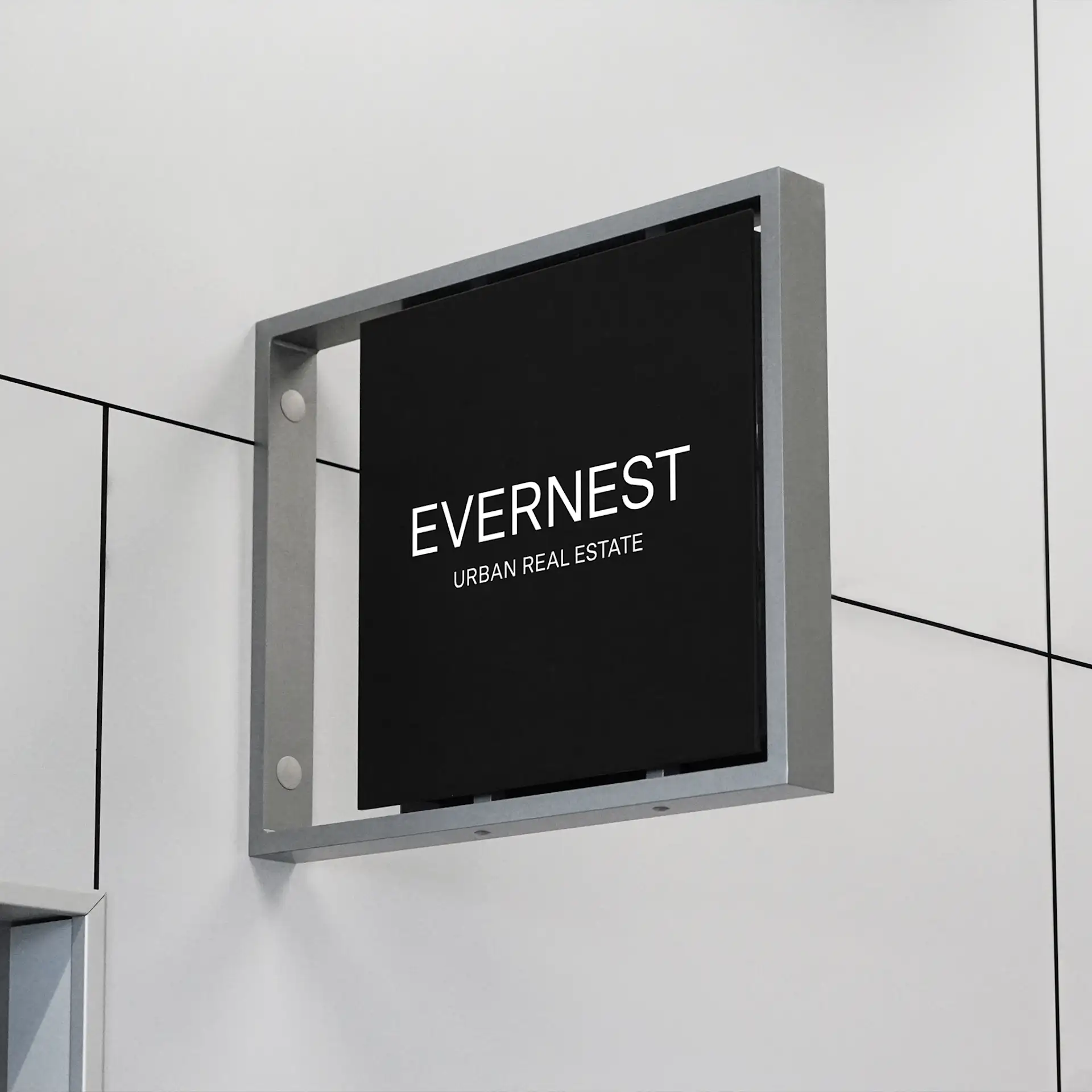 Schwarzes Schild mit weißer Aufschrift 'EVERNEST URBAN REAL ESTATE' an einer hellen Wand.
