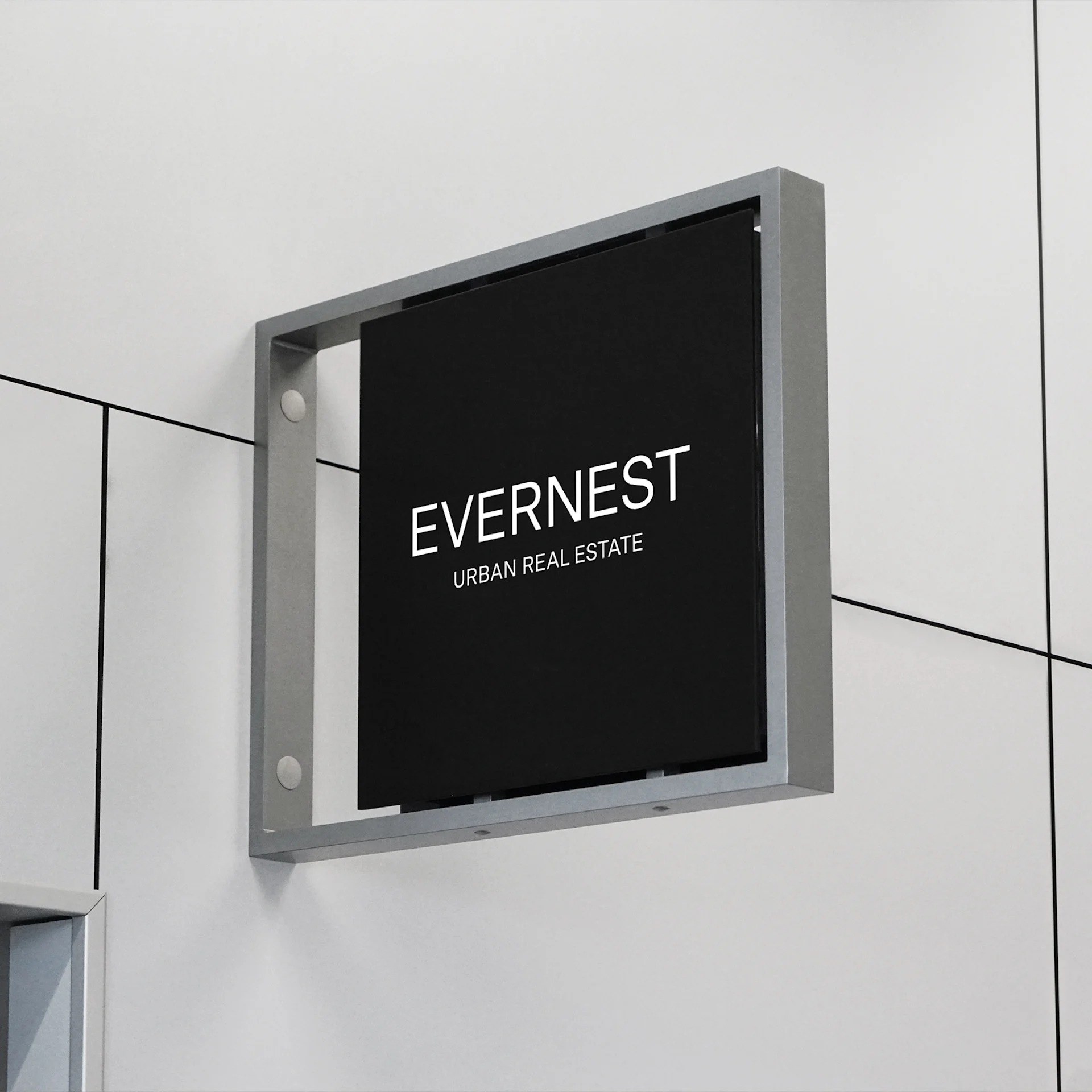Schwarzes Schild mit weißer Aufschrift 'EVERNEST URBAN REAL ESTATE' an einer hellen Wand.