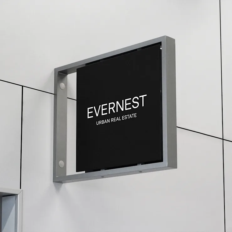 Schwarzes Schild mit weißer Aufschrift 'EVERNEST URBAN REAL ESTATE' an einer hellen Wand.