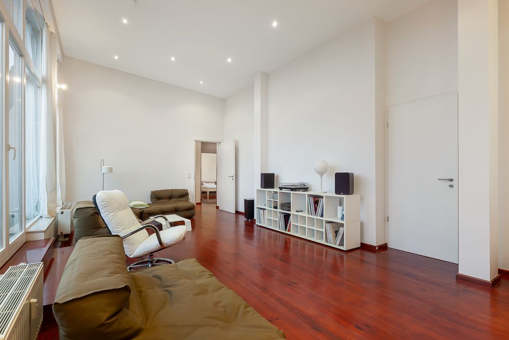 Modernes Wohnzimmer mit braunem Sofa, Sessel, Regalwand und Holzboden.