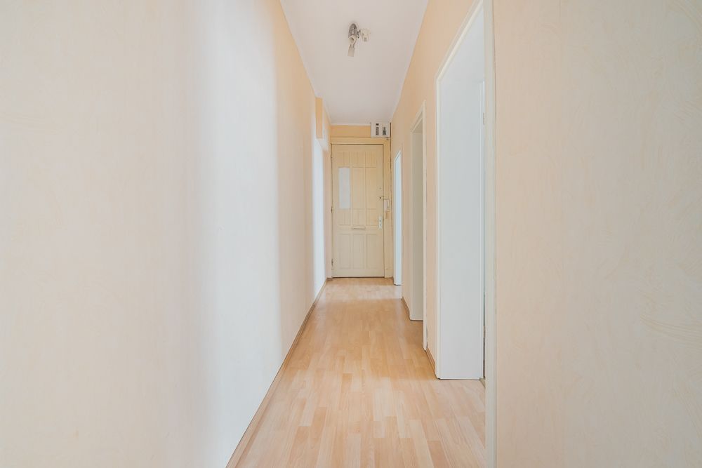 Heller Flur mit Holzboden, Türen zu mehreren Zimmern und einer geschlossenen Tür am Ende.