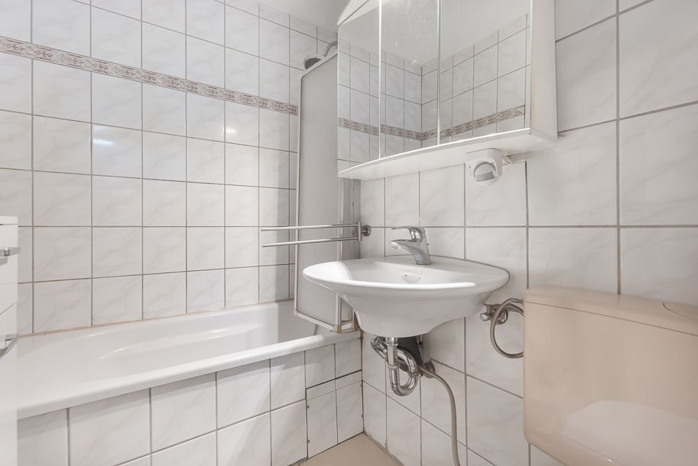 Helles Badezimmer mit Badewanne, Waschbecken, Spiegel und WC, weiße Fliesen an den Wänden.
