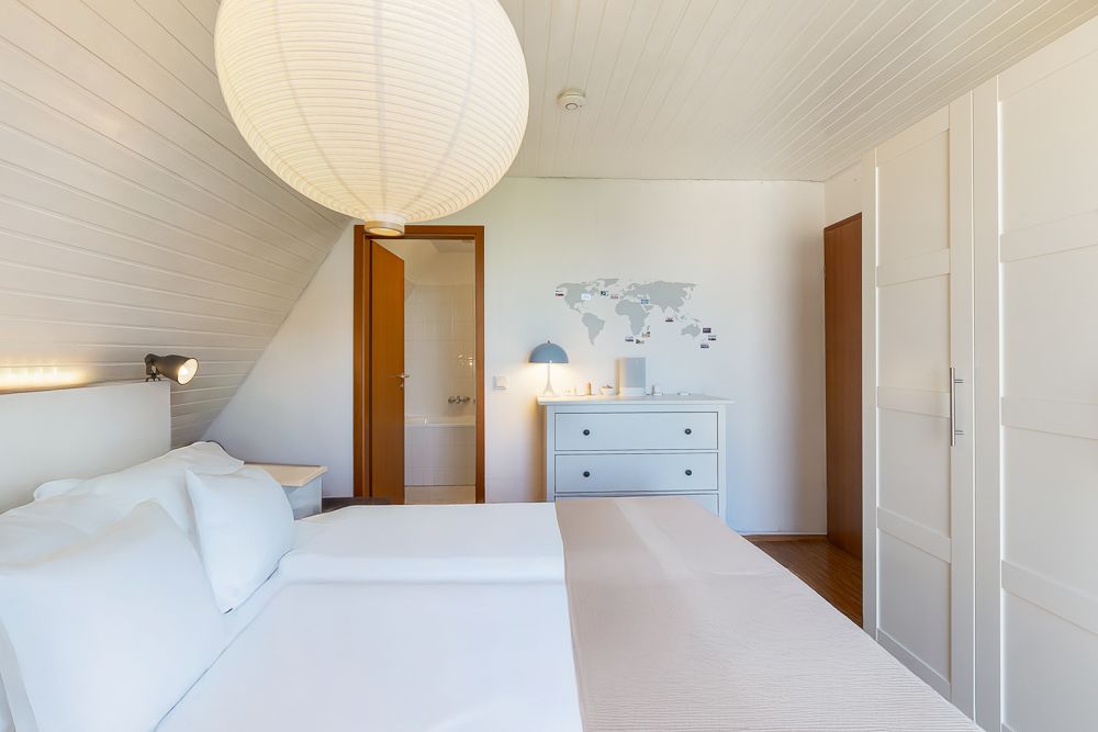 Helles Schlafzimmer mit Doppelbett, Kleiderschrank, Kommode und Weltkarte an der Wand.